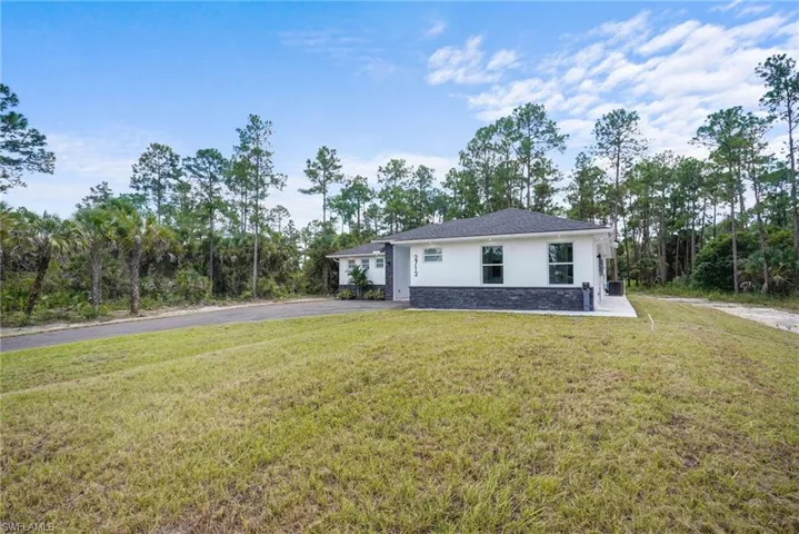 View of front of home with stucco siding, a front yard, stone siding, asphalt driveway, and view of wooded area