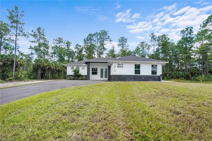 View of front of property with stucco siding, a front yard, stone siding, french doors, and view of scattered trees
