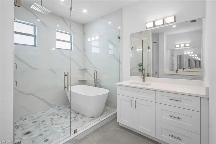 Primary Bathroom with a marble finish shower, a soaking tub, vanity, and light tile patterned floors