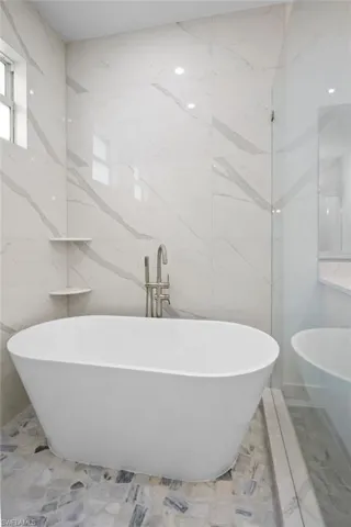 Primary Bathroom featuring a soaking tub, tile walls, marble tiled floors, and stone wall