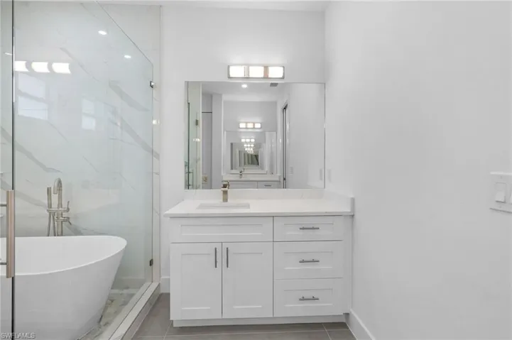Primary Bathroom with vanity, a freestanding bath, a marble finish shower, and light tile patterned floors