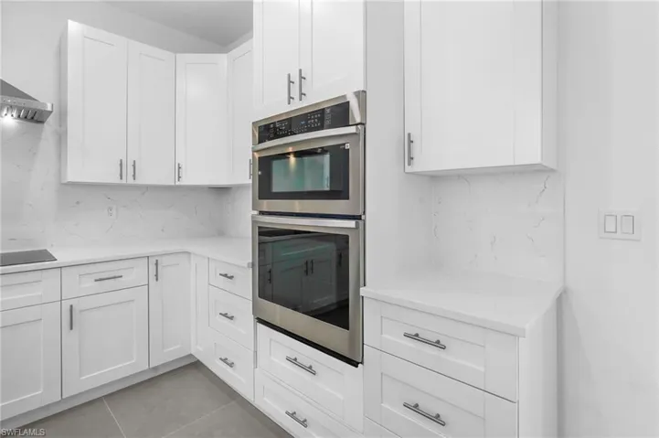 Kitchen featuring decorative backsplash, stainless steel double oven, light stone countertops, and white cabinetry