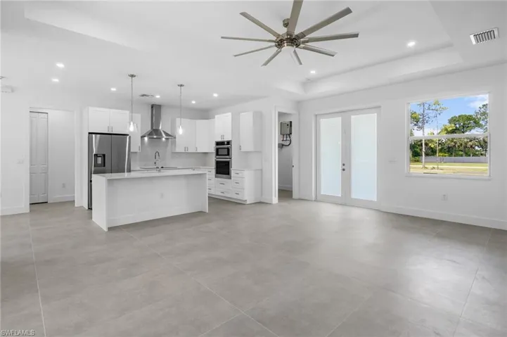 Unfurnished living room featuring french doors, a raised ceiling, recessed lighting, and ceiling fan