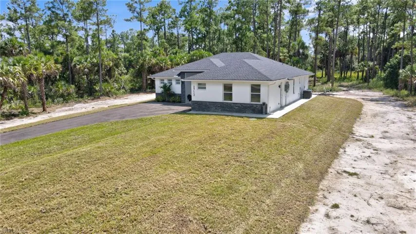 View of front of home with stucco siding, a front yard, a shingled roof, and asphalt driveway