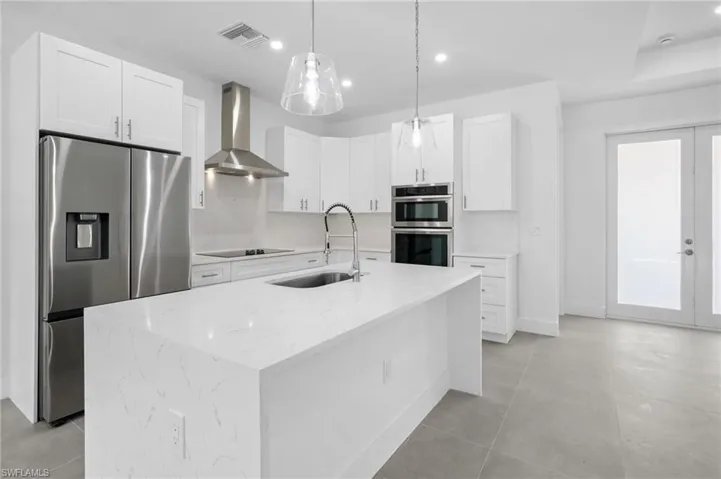 Kitchen featuring stainless steel appliances, wall chimney exhaust hood, white cabinets, light stone countertops, and decorative light fixtures