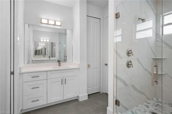 Bathroom with a marble finish shower, vanity, a closet, and dark tile patterned flooring