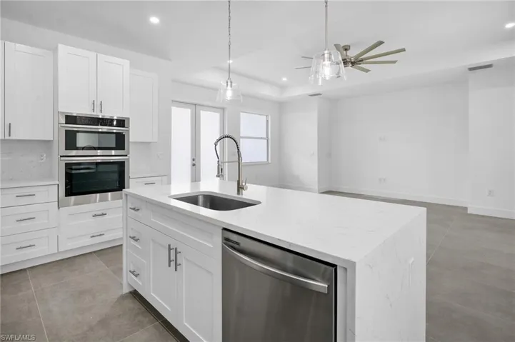 Kitchen featuring appliances with stainless steel finishes, light stone countertops, white cabinetry, a tray ceiling, and decorative light fixtures