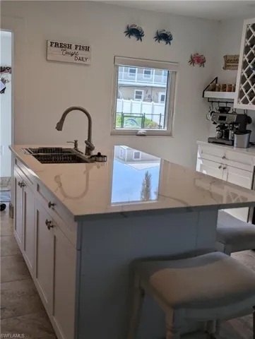 Kitchen featuring white cabinets, a center island with sink, light stone counters, and a breakfast bar