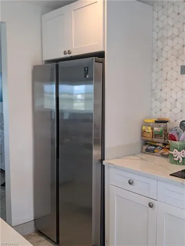 Kitchen with white cabinets, freestanding refrigerator, and light stone countertops