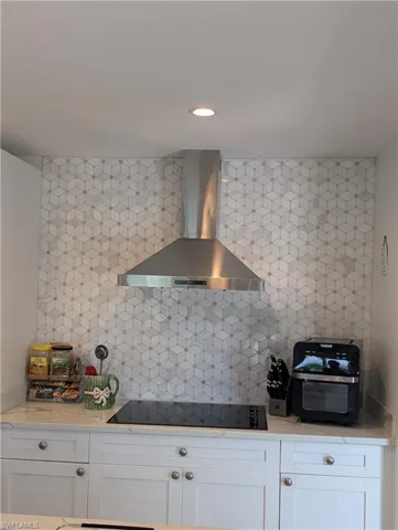 Kitchen with white cabinets, wall chiminey hood, decorative backsplash, light stone counters, and recessed lighting
