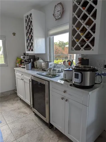 Bar area with white cabinetry, beverage cooler, healthy amount of natural light, and light tile patterned floors