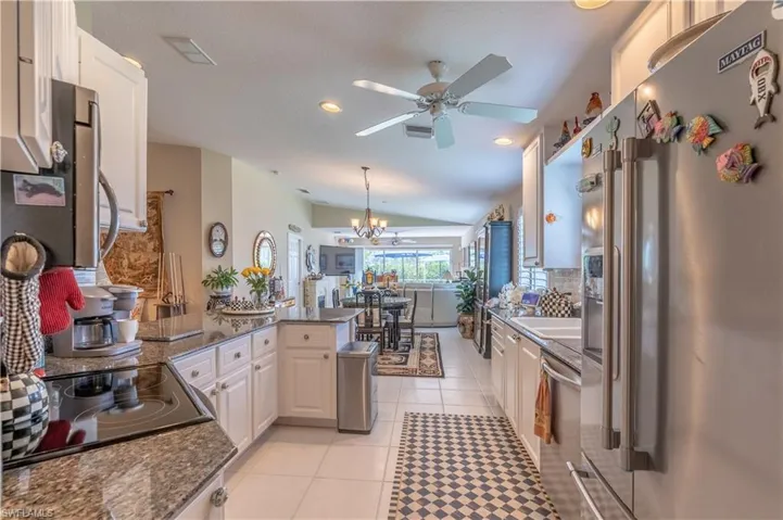 Kitchen with ceiling fan with notable chandelier, kitchen peninsula, white cabinetry, appliances with stainless steel finishes, and light tile floors