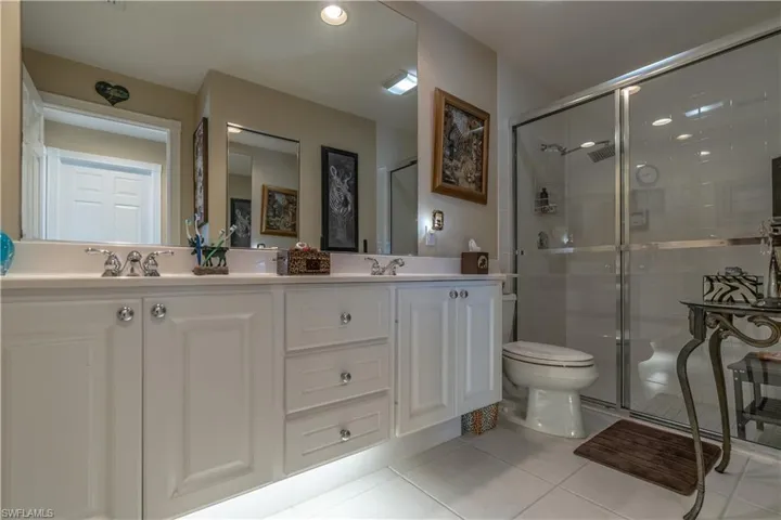 Bathroom featuring tile floors, dual sinks, vanity with extensive cabinet space, and walk in shower