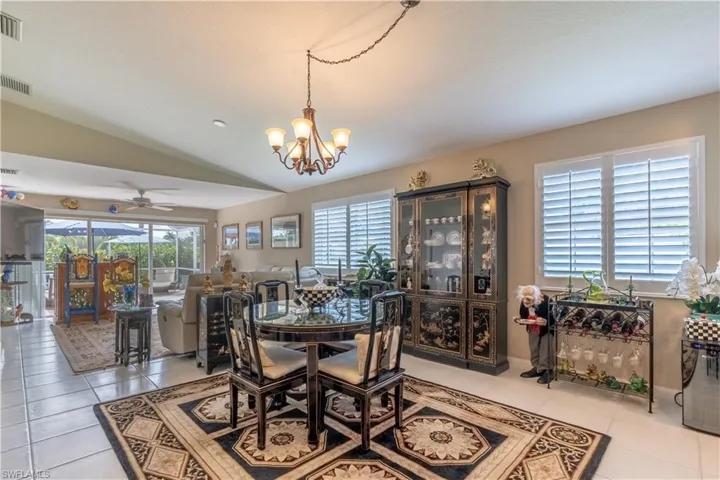Dining room featuring light tile flooring, vaulted ceiling, and ceiling fan with notable chandelier