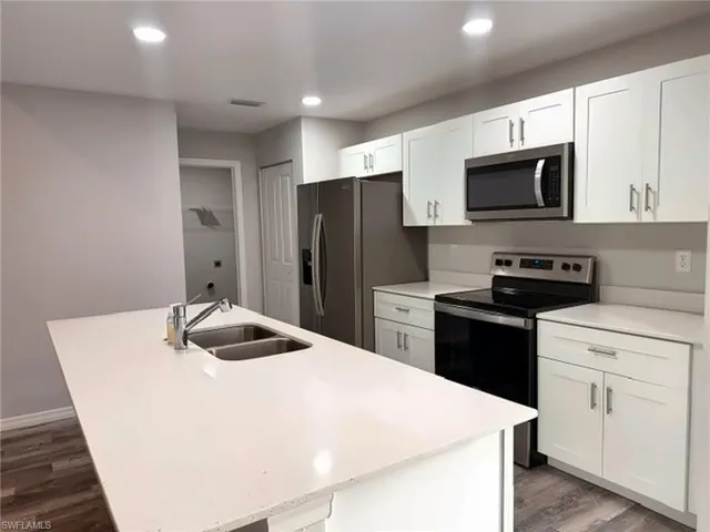 Kitchen featuring white cabinetry, stainless steel appliances, wood-finish flooring, recessed lighting, and a kitchen island with an integrated double sink