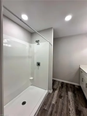 Primary bathroom featuring a walk-in shower with a white surround and chrome fixtures, wood-finish flooring, white vanity with integrated countertop, and recessed ceiling lighting
