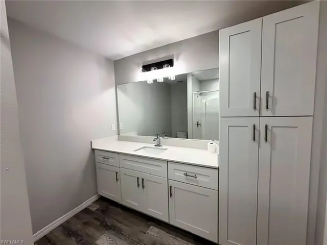 Primary bathroom with white shaker-style cabinetry with dark hardware, a white countertop, an integrated sink, and wood-finish flooring
