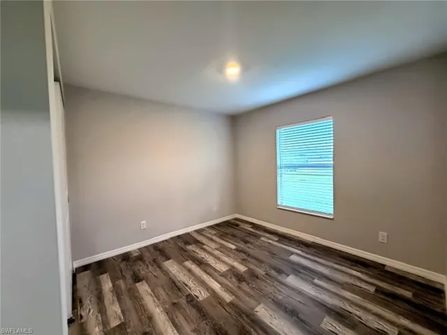 Primary bedroom with neutral wall color, wood-finish flooring, and window with horizontal blinds