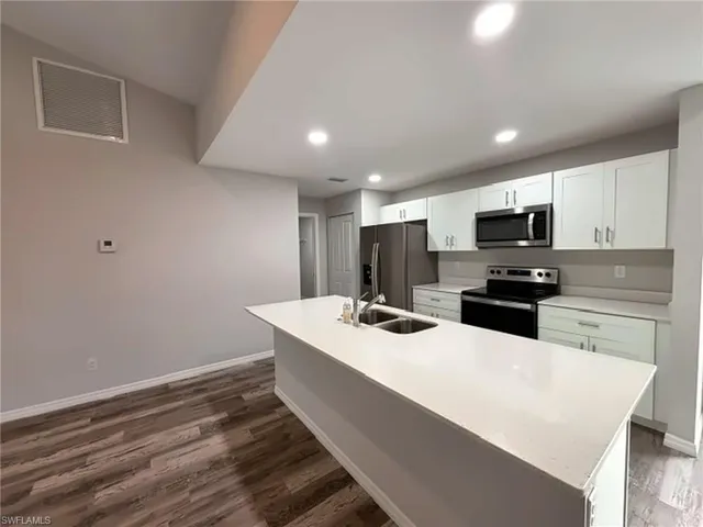 Kitchen featuring an island with a dual-basin stainless steel sink, wood-finish flooring, white cabinetry, stainless steel appliances, and recessed lighting