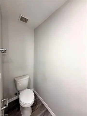 Private water closet in the primary bathroom featuring a toilet, wood-finish flooring, and an exhaust fan