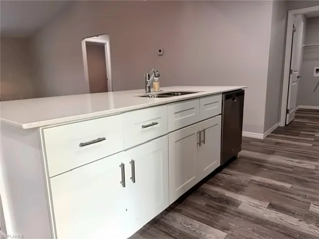 Kitchen island featuring white cabinetry, a double basin sink with a chrome faucet, stainless steel dishwasher, and a white countertop