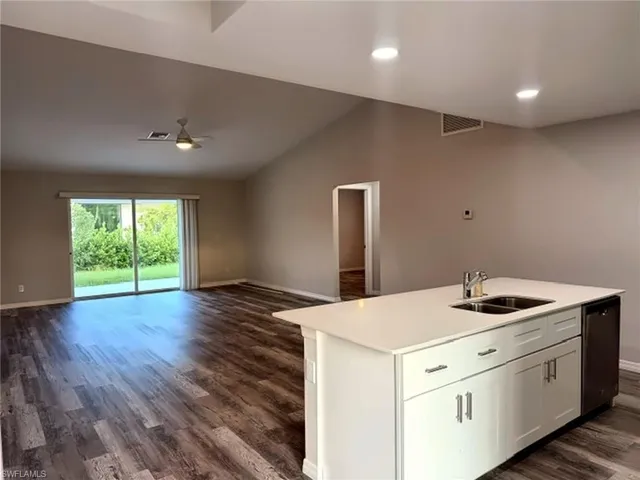 Vaulted ceiling, wood-finish flooring, white kitchen island with sink, stainless steel dishwasher, and sliding glass doors to the exterior