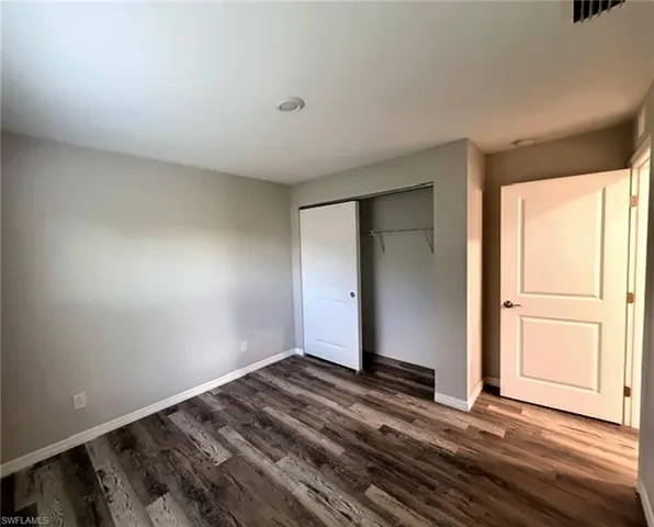 Recessed ceiling lighting, wood-finish flooring, sliding closet doors, built-in closet shelving, and a panel door with dark hardware