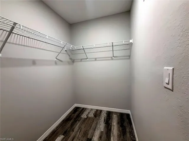 Primary walk-in closet with white wire shelving system, light gray wall finish, and wood-finish flooring