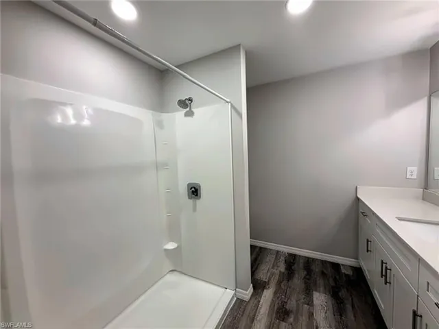 Primary bathroom featuring a walk-in shower with chrome fixtures, vanity with integrated sink, quartz-finish countertop, white cabinetry with dark pulls, and wood-finish flooring