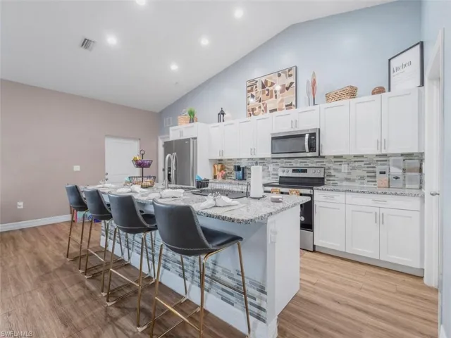 Kitchen featuring a breakfast bar, appliances with stainless steel finishes, white cabinets, light stone countertops, and recessed lighting