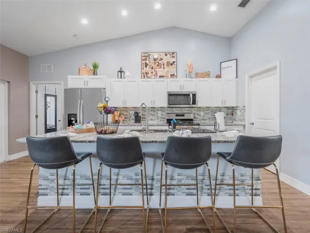 Kitchen featuring white cabinetry, a kitchen breakfast bar, backsplash, an island with sink, and stainless steel appliances