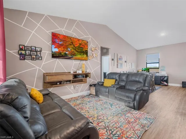 Living area featuring an accent wall, vaulted ceiling, wood finished floors, and recessed lighting