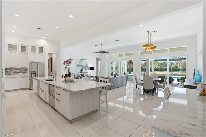 Kitchen featuring a breakfast bar, glass insert cabinets, light stone counters, hanging light fixtures, and a large island