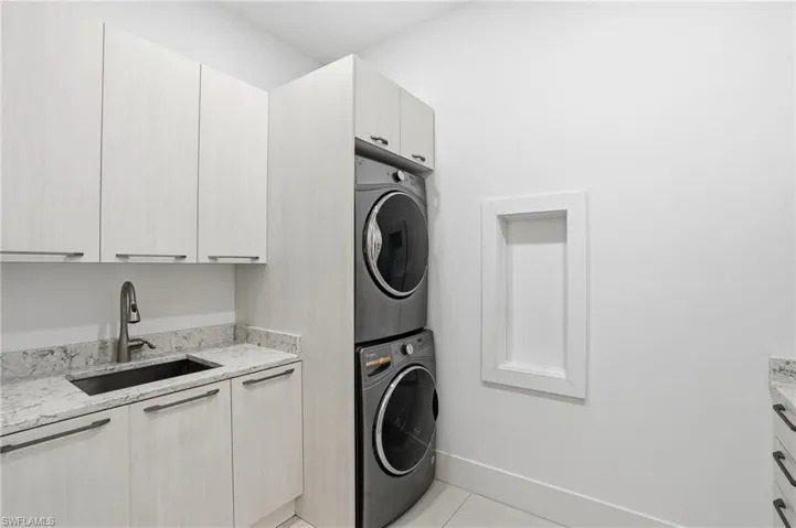 Laundry area with cabinet space, stacked washing machine and dryer, and light tile patterned floors