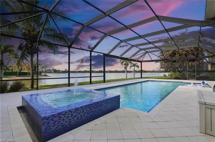 Pool at dusk with a water view, a pool with connected hot tub, and a lanai