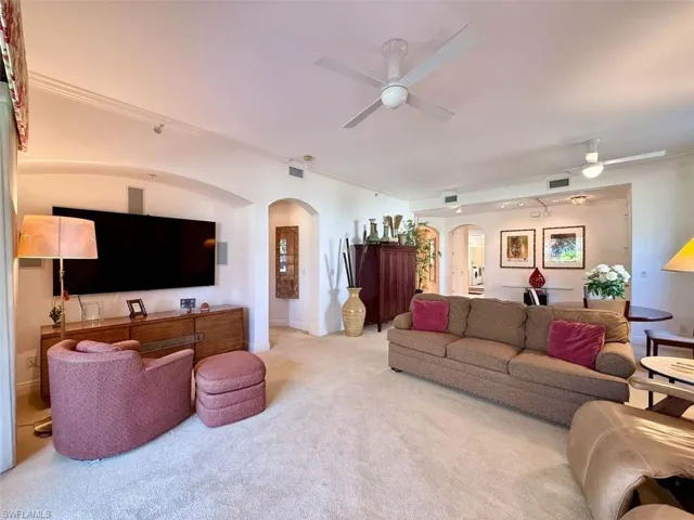 Living area featuring crown molding, carpet, arched walkways, ceiling fans