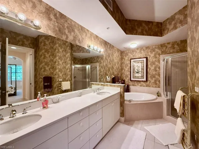 Full bath with a towel warmer, stall shower, tile patterned floors, dual sinks, and a garden tub