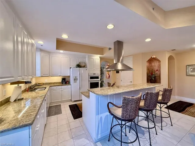 Kitchen featuring island exhaust hood, a breakfast bar, recessed lighting, a sink, and white refrigerator with ice dispenser