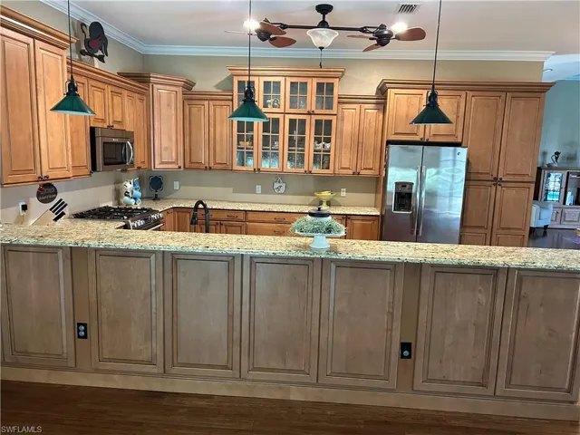Kitchen featuring decorative light fixtures, light stone counters, crown molding, and appliances with stainless steel finishes