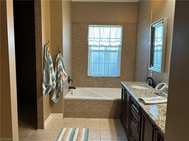 Bathroom with tile patterned flooring, vanity, and a relaxing tiled tub