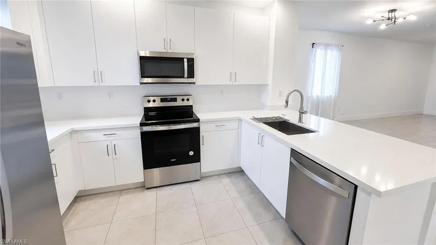 Modern kitchen featuring white cabinetry, stainless steel appliances, a deep basin sink with a gooseneck faucet, light-toned countertop, and tile flooring