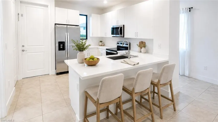 Modern kitchen featuring a white countertop island with seating, stainless steel appliances, white cabinetry, and tiled flooring
