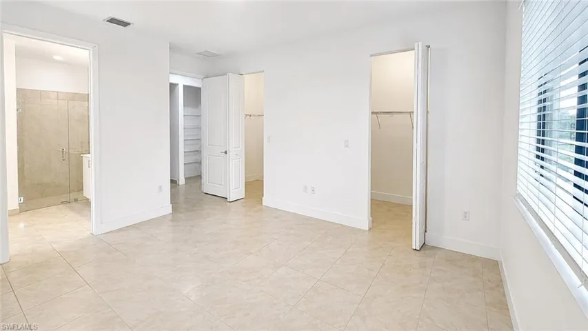 Spacious room with light-toned large format floor tiling, crisp white walls, and a large window with horizontal blinds