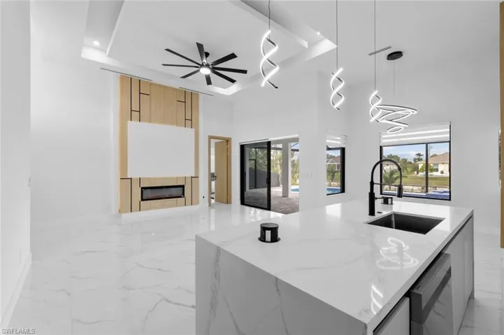 Kitchen with a raised ceiling, a kitchen island with sink, light stone counters, and pendant lighting