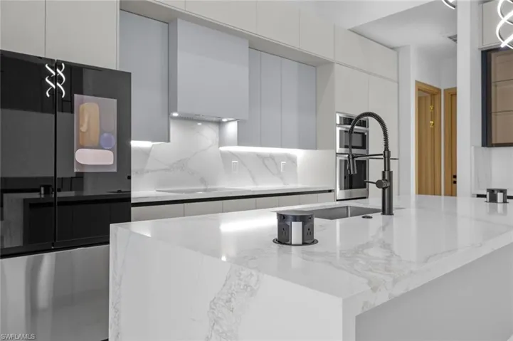 Kitchen with decorative backsplash, cooktop, light stone countertops, white cabinets, and double oven