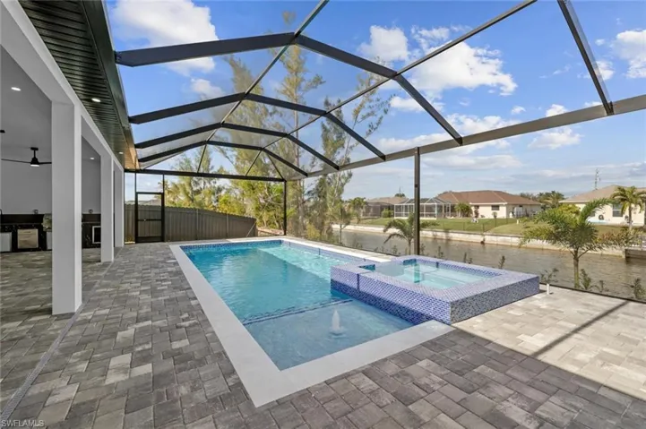 View of swimming pool with a lanai, a water view, a patio area, and an in ground hot tub