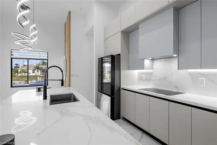 Kitchen featuring white cabinetry, decorative backsplash, light stone countertops, black appliances, and sink