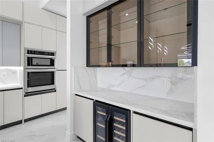 Kitchen with light stone countertops, white cabinets, double oven, and wine cooler
