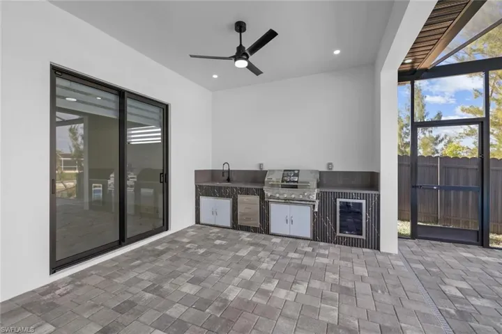 View of patio featuring ceiling fan, area for grilling, sink, glass enclosure, and grilling area