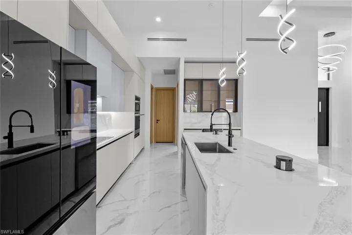 Kitchen with light stone countertops, white cabinetry, hanging light fixtures, and sink
